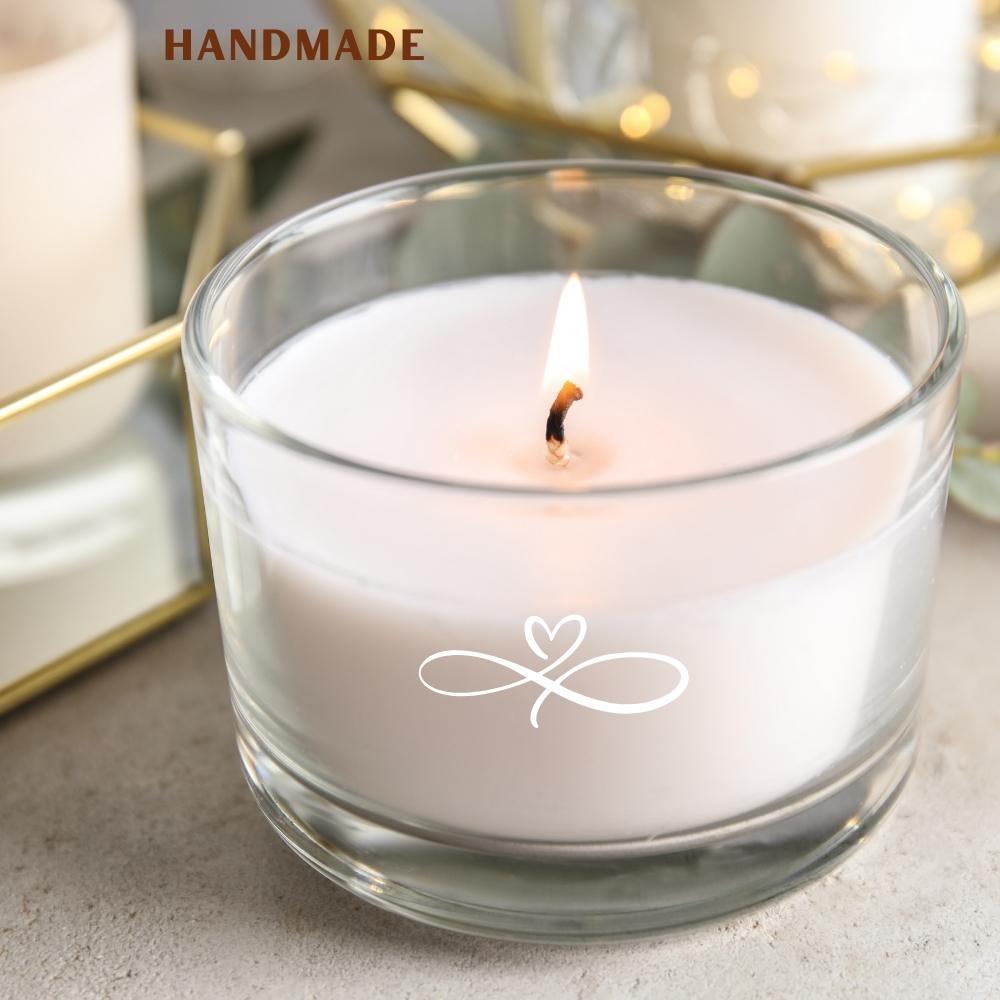 Handmade candle in a glass container with a lit wick on a neutral background