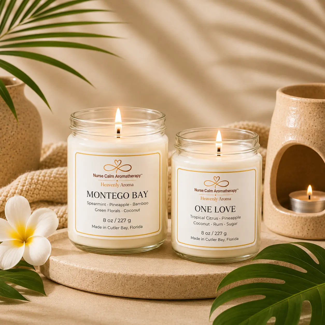 Tropical Escape Collection lifestyle photo featuring the One Love and Montego Bay luxury soy candles displayed in a warm tropical-inspired spa setting with palm leaves, soft candlelight, and neutral coastal décor.
