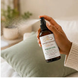 Hand using Focus Fuel Room & Linen Spray to refresh a room with a botanical mist.