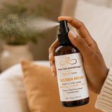 Hand using Golden Hour Room & Linen Spray to refresh a room with a botanical mist.