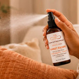 Hand using Sunset Escape Room & Linen Spray to refresh a room with a botanical mist.