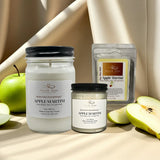 Two jars of 'Apple Martini' candle, a package of candles, and apples on a beige surface.