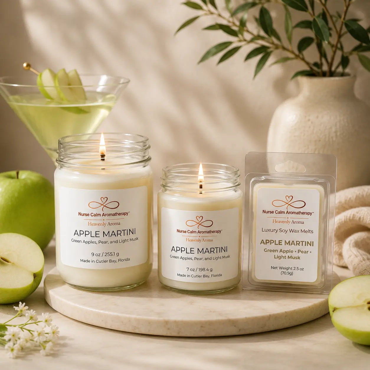 Three candles labeled 'Apple Martini' on a wooden board with apples and a martini glass in the background.