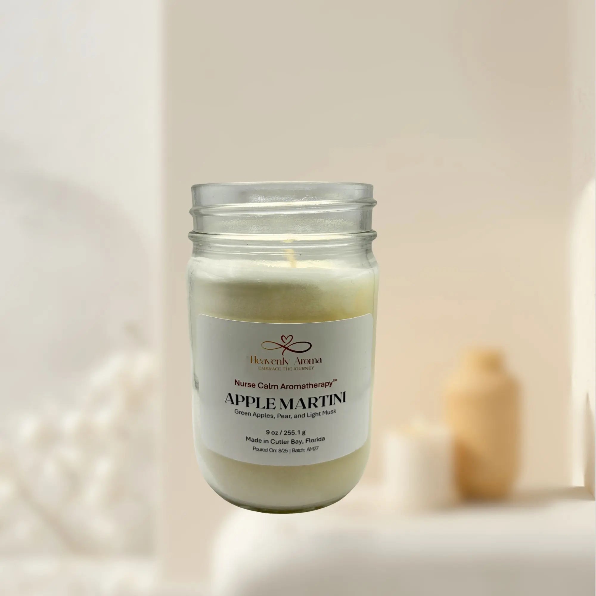 Candle in a glass jar labeled 'Apple Martini' with a soft background