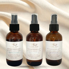 Three amber glass bottles with black spray nozzles on a textured beige background