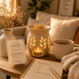 Cozy wellness scene featuring Butter Shot Luxury Soy Wax Melts, a glowing wax warmer, warm tea, soft blankets, and relaxing home décor for a peaceful self-care experience.