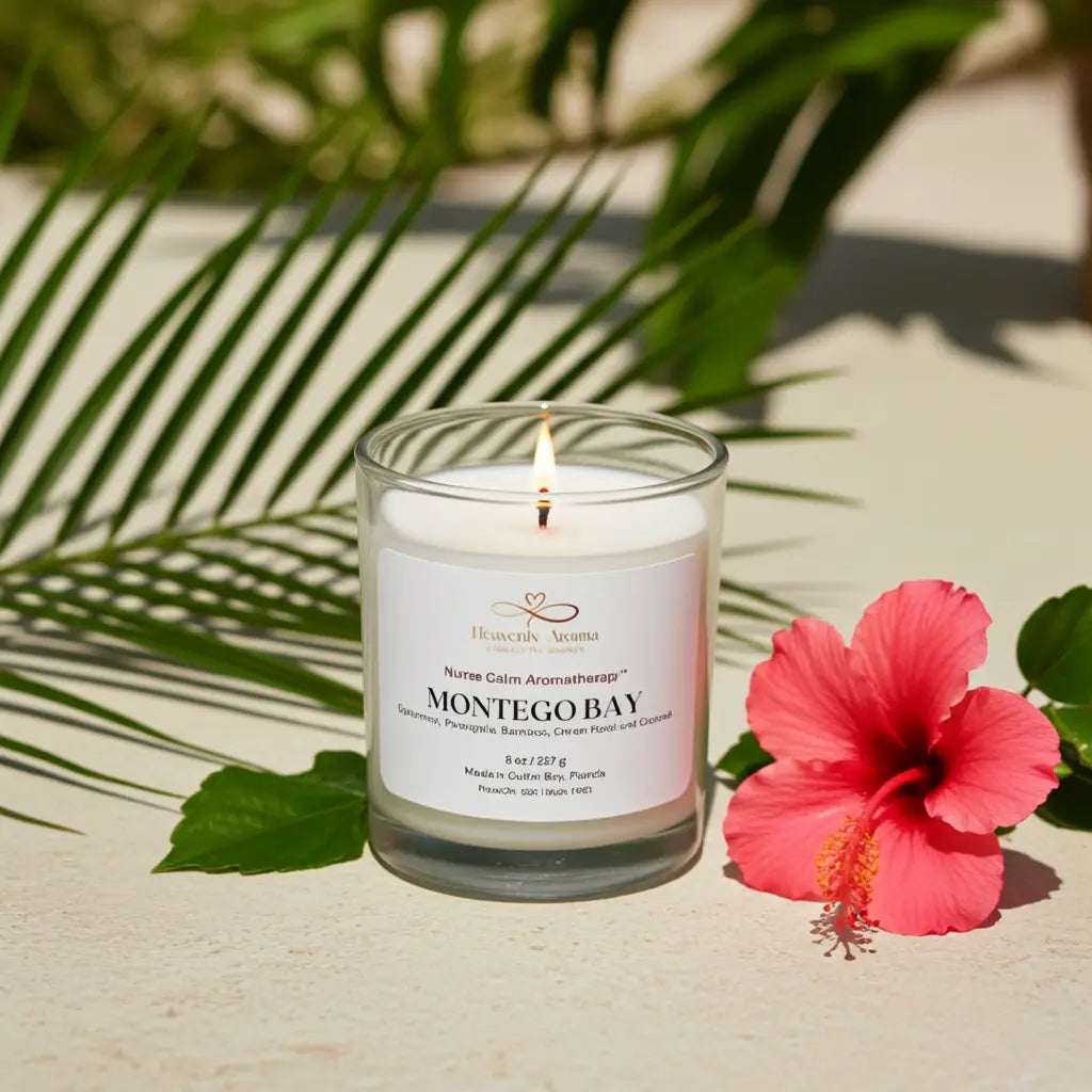 Candle in a glass jar with a label, surrounded by green leaves and a pink flower on a light surface.
