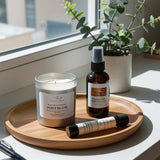 Candle, bottle, and tube on a wooden tray with a plant in the background