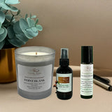 Candle, spray bottle, and roller bottle with labels on a beige surface next to a plant.