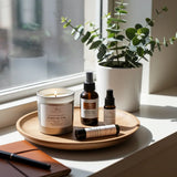 Candle and skincare products on a wooden tray with a plant in the background