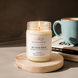 Butter Shot soy candle glowing beside a coffee mug in a warm, relaxing home setting.