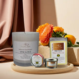 Candle and packaging with 'ONELOVE' branding on a wooden tray with flowers in the background.