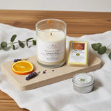 Candle, packaging, and small container on a wooden board with a white cloth background