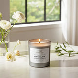 Candle with a label on a table near flowers and a window