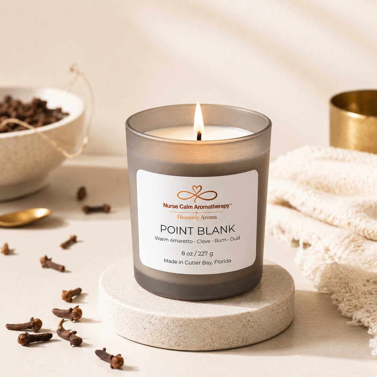 Candle labeled 'Point Blank' from Nurse Calm Aromatherapy on a neutral background with clove spices.