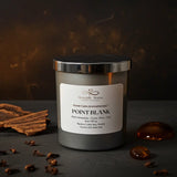Candle labeled 'Point Blank' from Heavenly Aroma on a dark surface with cinnamon sticks and spices.