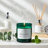 Green candle labeled 'Sensaytional' with diffuser and eucalyptus leaves on a white surface