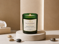Sensaytional soy candle by Nurse Calm Aromatherapy™ displayed on a neutral cream pedestal with soft spa-inspired décor. Green glass candle with gold-trimmed label and lit flame featuring peppermint, eucalyptus, cedarwood, and vanilla fragrance notes.
