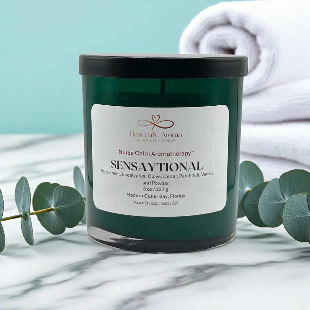 Candle labeled 'Sensaytional' by Heavenly Aroma on a marble surface with eucalyptus leaves and a towel in the background.