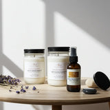 Three candles and a bottle of essential oil on a wooden table with lavender flowers.