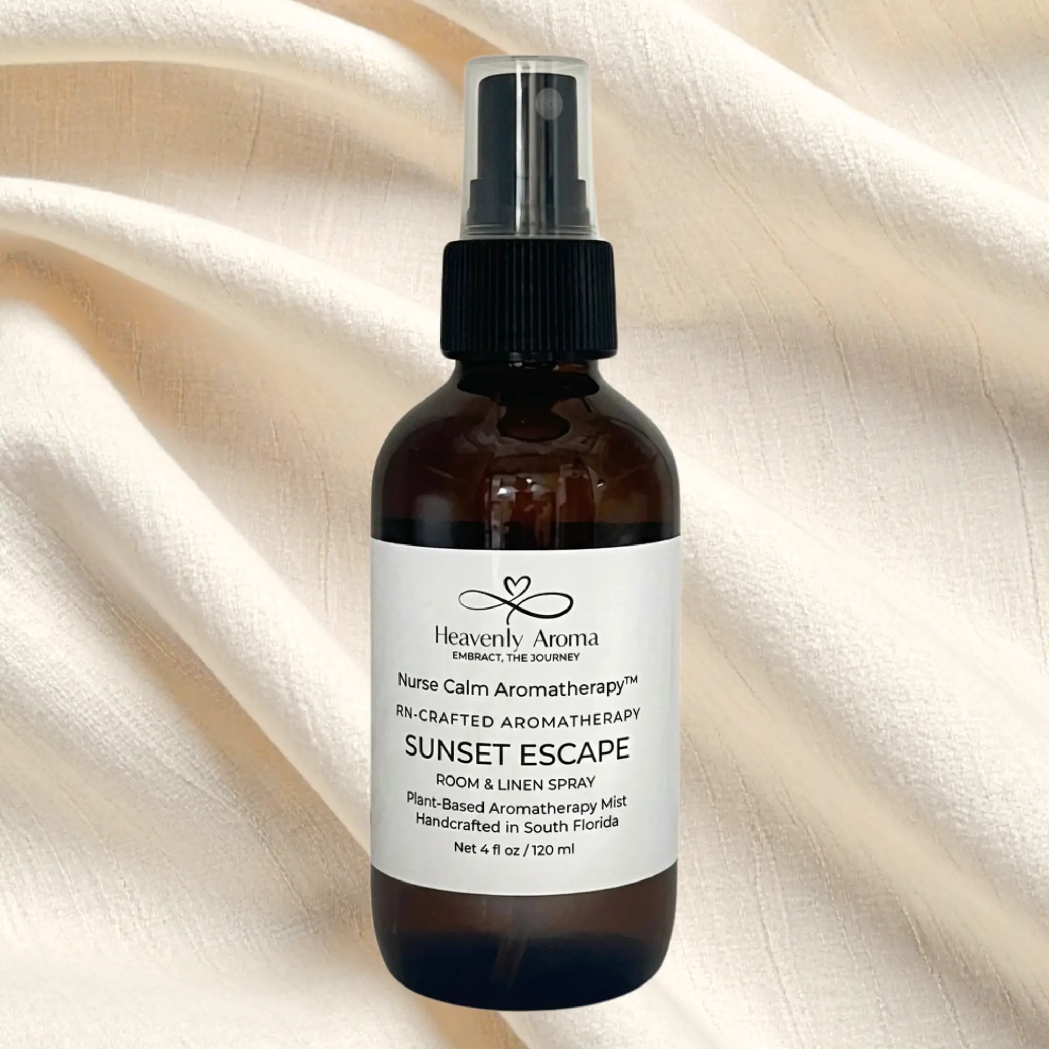 Bottle of 'Sunset Escape' room & linen spray by Heavenly Aroma on a beige fabric background