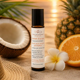 Essential oil roller bottle labeled 'Sunset Escape' with tropical elements like a pineapple, coconut, and orange on a sandy background.