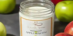 Apple martini scented candle in a clear glass jar with white wax and orange label.