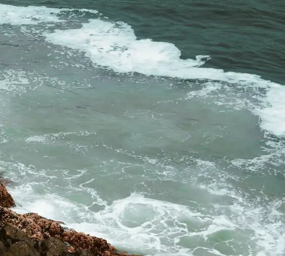 Foamy turquoise ocean waves crashing against dark, rugged rocks