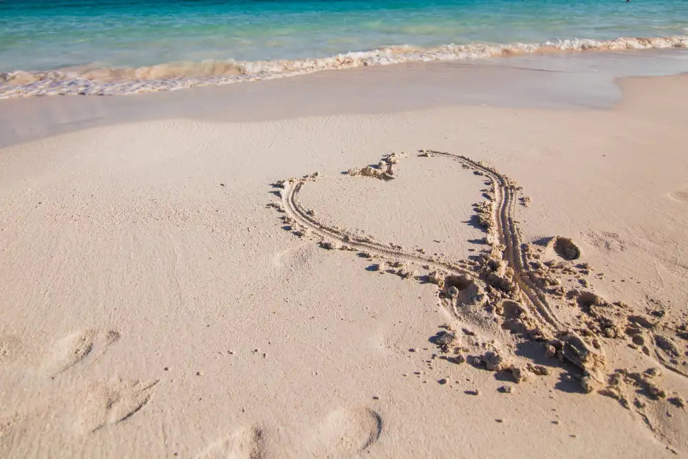 A heart drawn in the sand on a sunny beach.