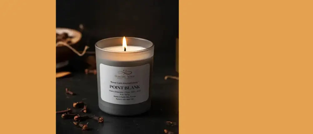 A lit, gray glass candle with a white label reading ’point blank’ sits on a dark surface.