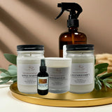 Collection of natural products including candles and a spray bottle on a gold tray with a neutral background.